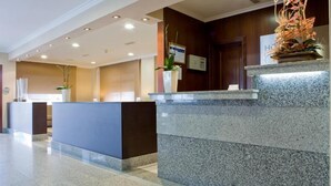 A hotel reception area with a marble reception desk, potted plants, and a wooden wall. - Duna Hotel (Sanxenxo)