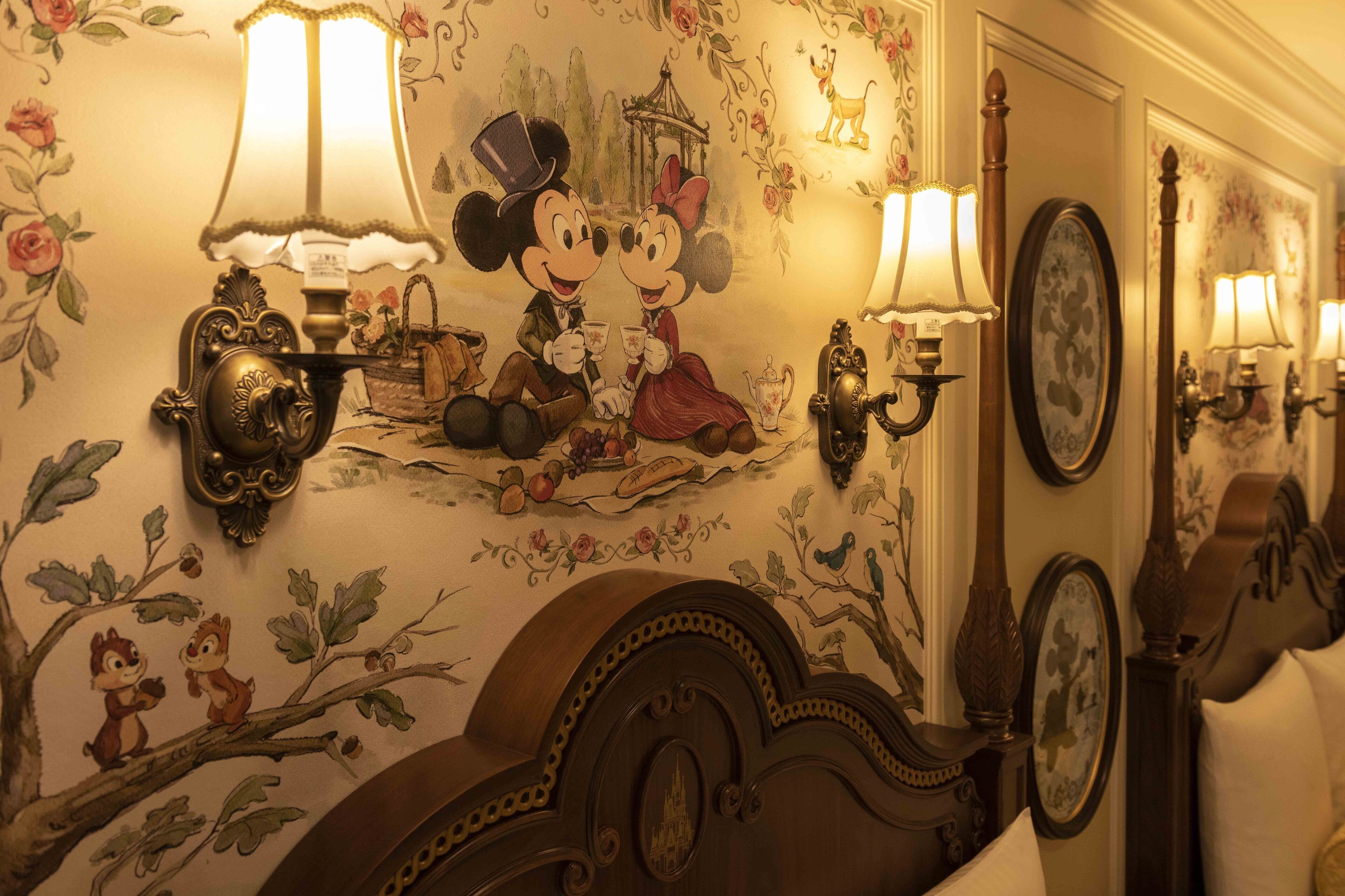 A room with a mural of Mickey and Minnie Mouse, ornate wall sconces, and a classic bed with a carved headboard.