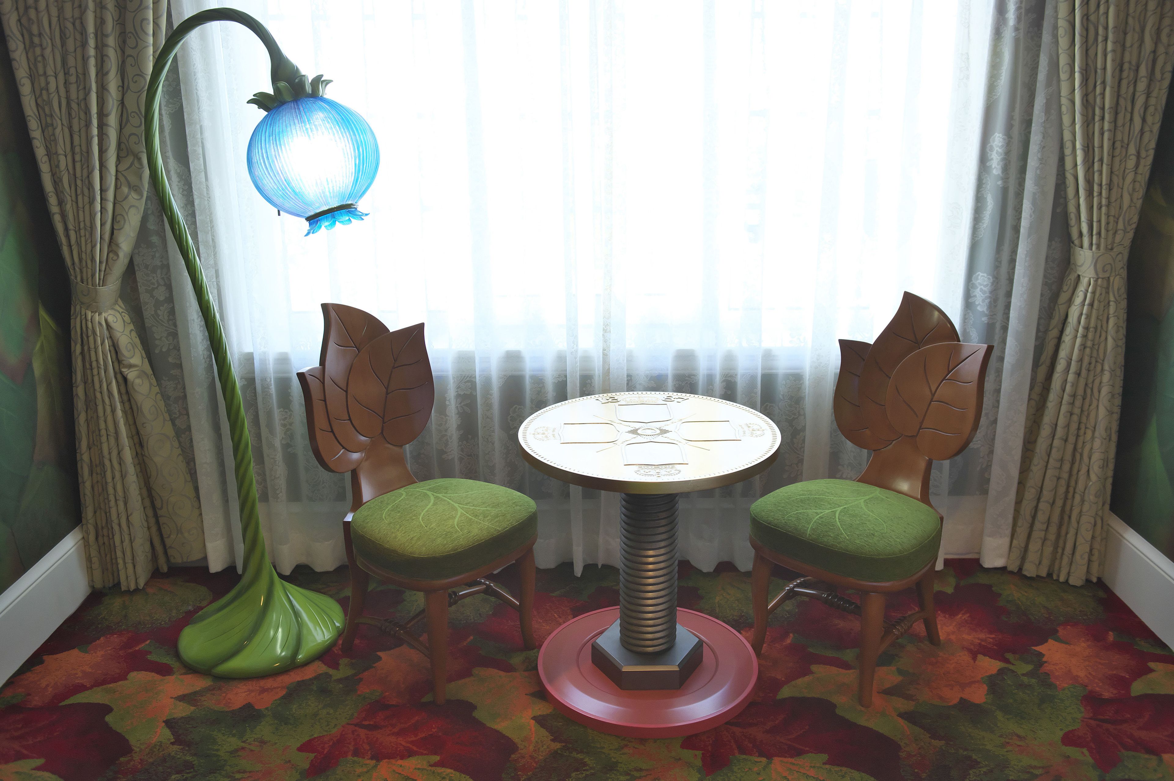 A room with a round table, two chairs, a green floor lamp, and a window with curtains.