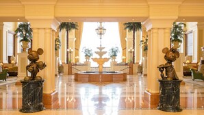 A lobby with marble floors, a central fountain, and two Mickey Mouse statues on pedestals.