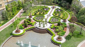 Een aangelegde tuin met een centrale fontein, omgeven door zorgvuldig gesnoeide hagen en bomen.