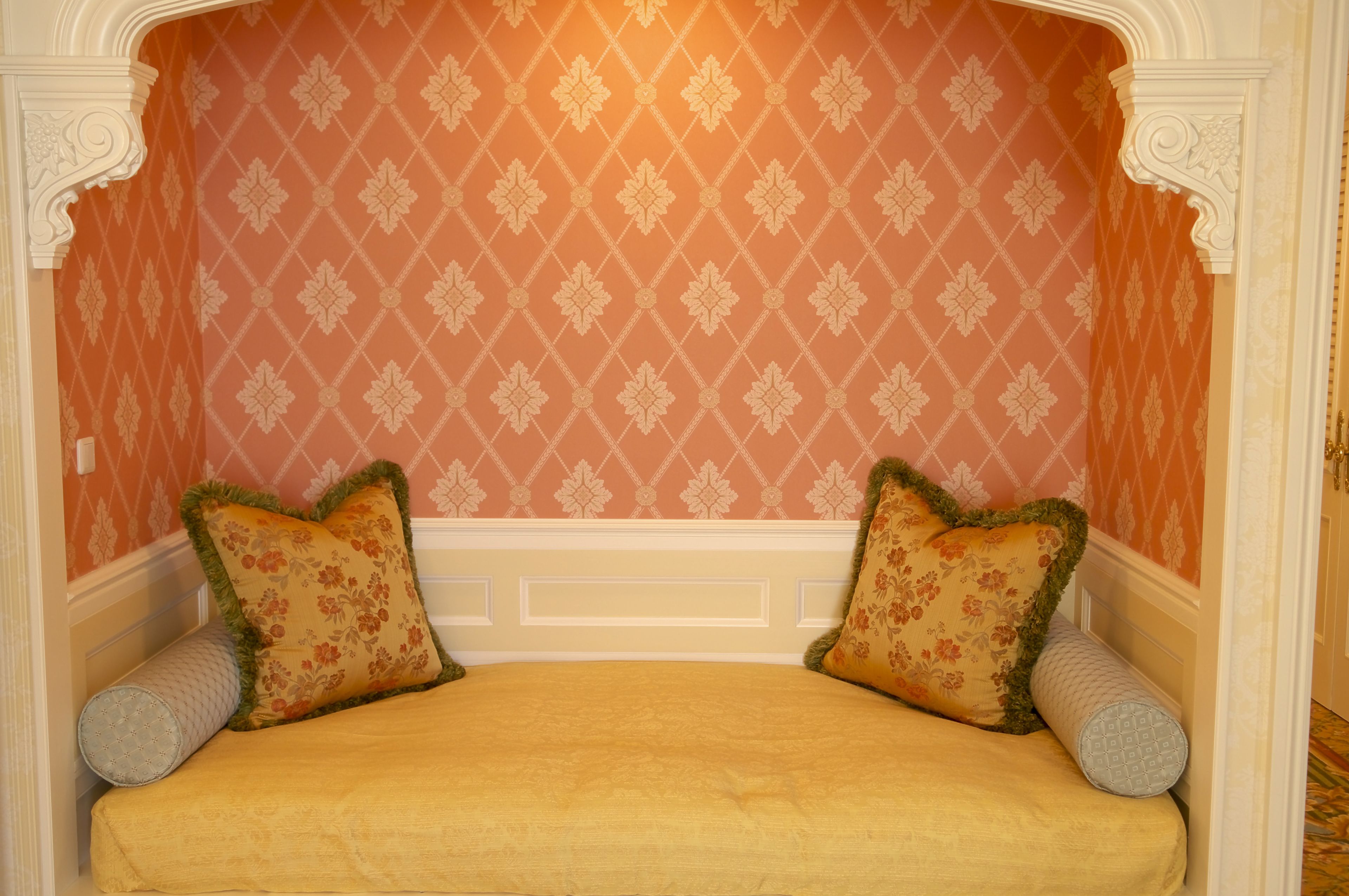 A bed with floral-patterned pillows and a yellow bedspread, set against a patterned wall with a white trim.
