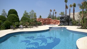 A swimming pool with a clear blue mosaic design, surrounded by palm trees and a rocky landscape.
