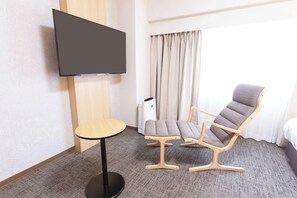 A hotel room with a flat-screen TV mounted on the wall, a round table, two cushioned chairs, a bed, and a window with curtains. - Toyama Chitetsu Hotel (Toyama)