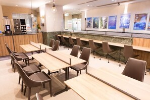 A conference room with multiple tables and chairs, a kitchenette area, and a wall with posters. - Toyama Chitetsu Hotel (Toyama)