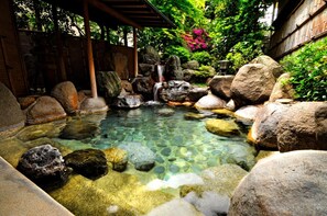 A clear water feature with rocks and a small waterfall, surrounded by lush greenery and a wooden structure. - Izumokamigami Enmusubi No Yado Konya (Matsue)