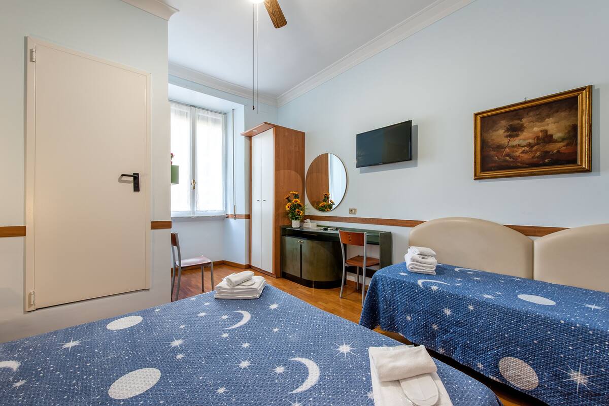 Ein Hotelzimmer mit zwei Betten, einem Schreibtisch, einem Sessel, einem Fernseher und einem Bild an der Wand.
