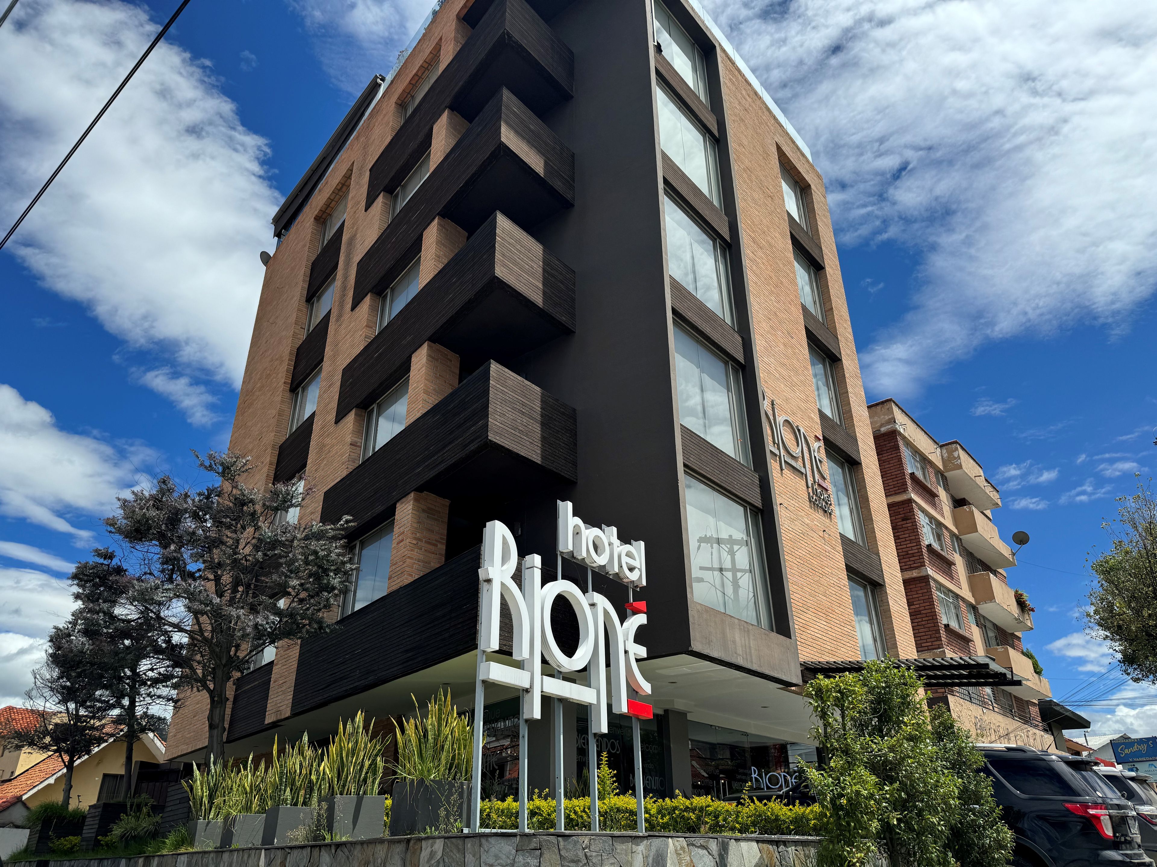 Un hotel llamado 'hotel one' con un diseño moderno, que presenta un letrero llamativo, varios balcones y una vista despejada del cielo.