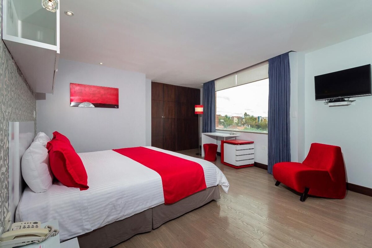 A hotel room with a bed, a desk, a chair, a TV, and a window with a view.