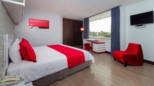 Una camera d'albergo con un letto, una scrivania, una sedia, una TV e una finestra con vista.