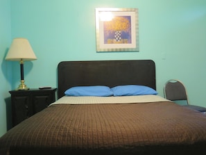Ein Schlafzimmer mit einem Bett, einer Lampe, einem Sessel und einem gerahmten Bild an der Wand.