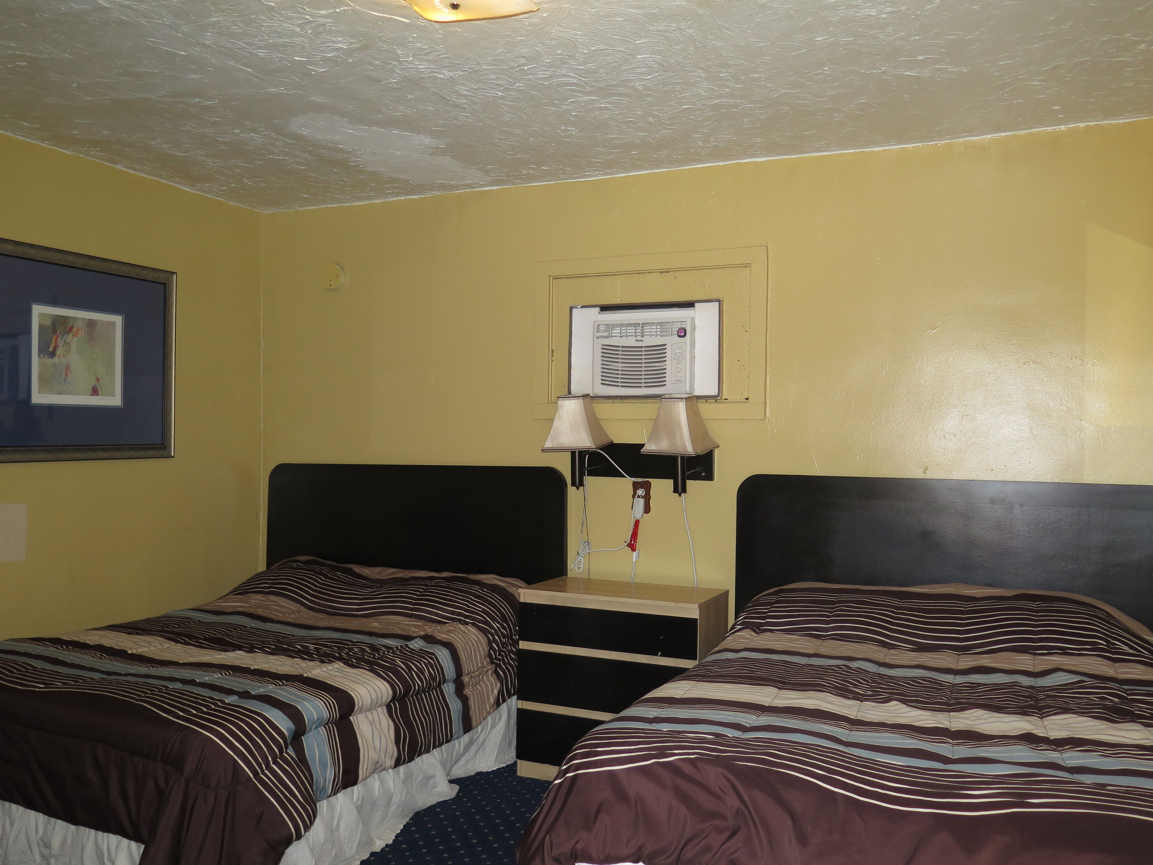 A room with two beds, a small desk, a wall-mounted air conditioner, and a framed picture.