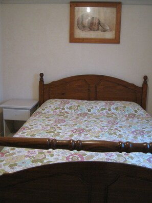 A bedroom with a wooden headboard, a floral bedspread, a nightstand, and a framed picture on the wall.