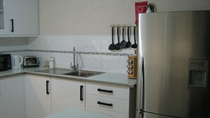 A kitchen with white cabinets, a stainless steel refrigerator, a microwave, a toaster, and a sink. - Princess Apartment (Mangrove)