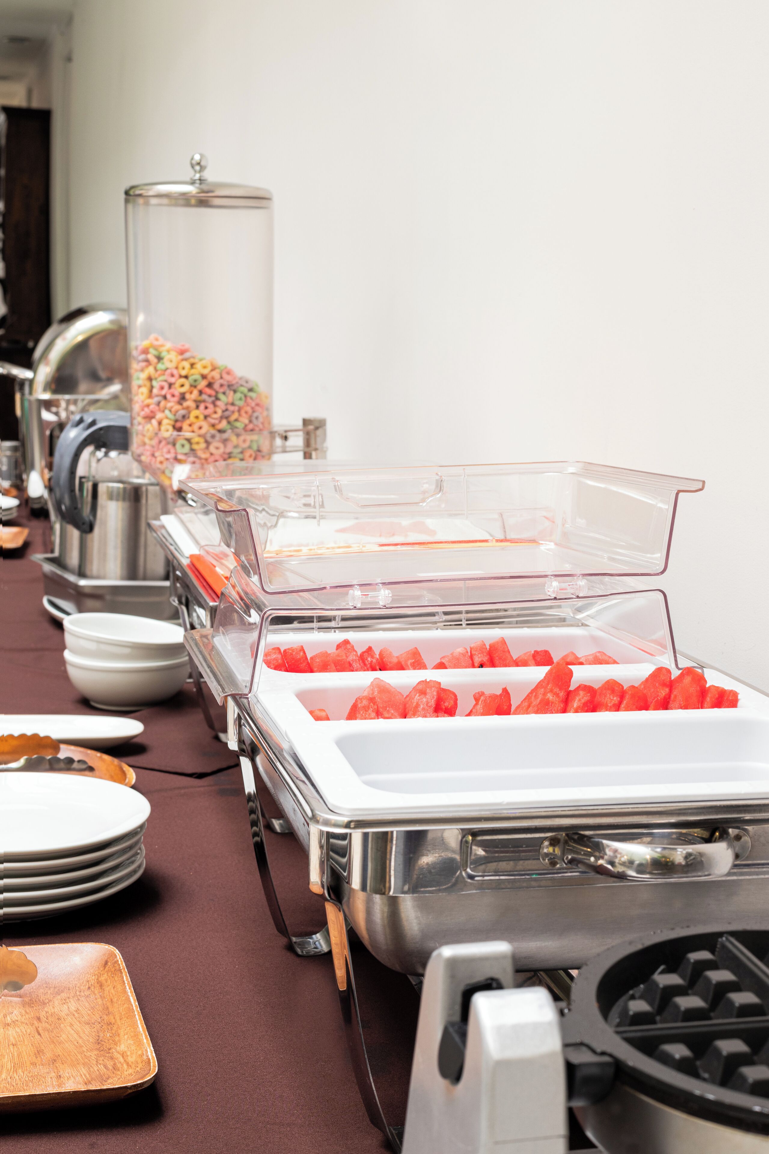 A buffet setup with clear plastic containers holding various food items, including watermelon and cereal.