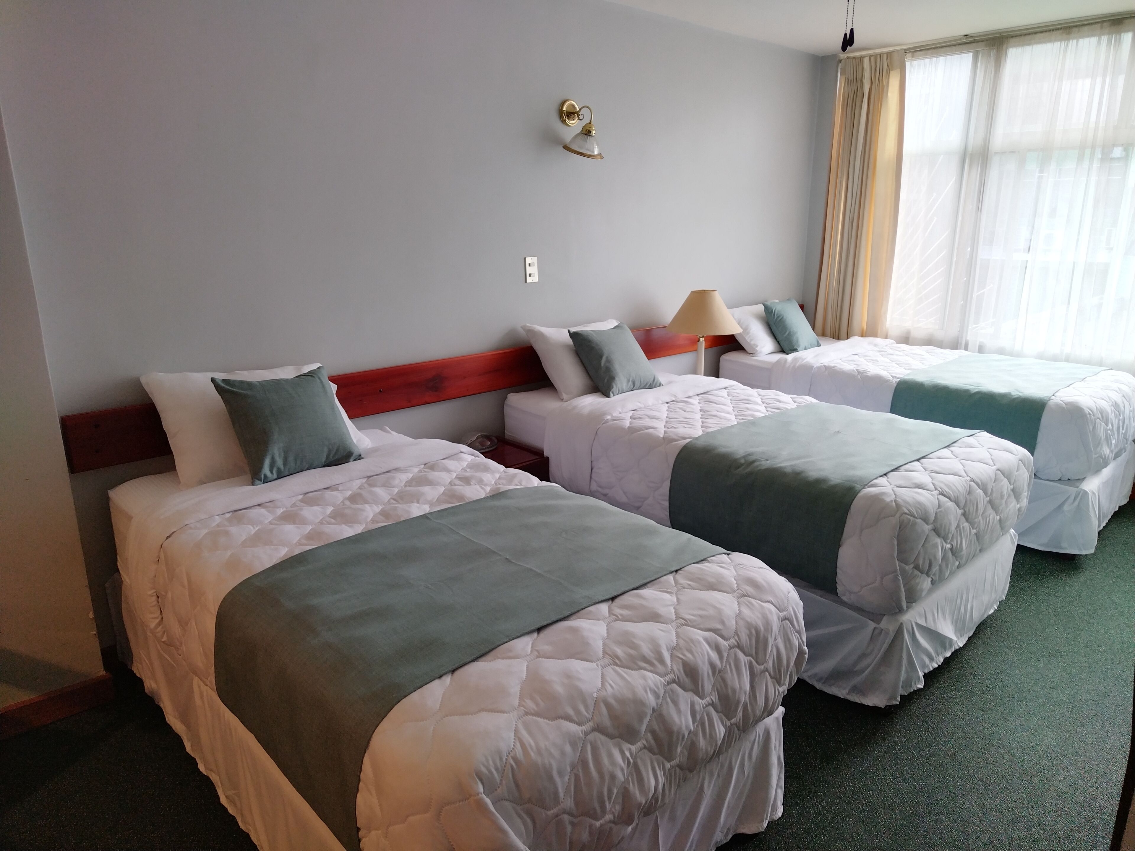 A hotel room with two beds, a wooden headboard, a lamp, and a window with curtains.