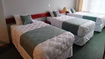 A hotel room with two beds, a wooden headboard, a lamp, and a window with curtains.