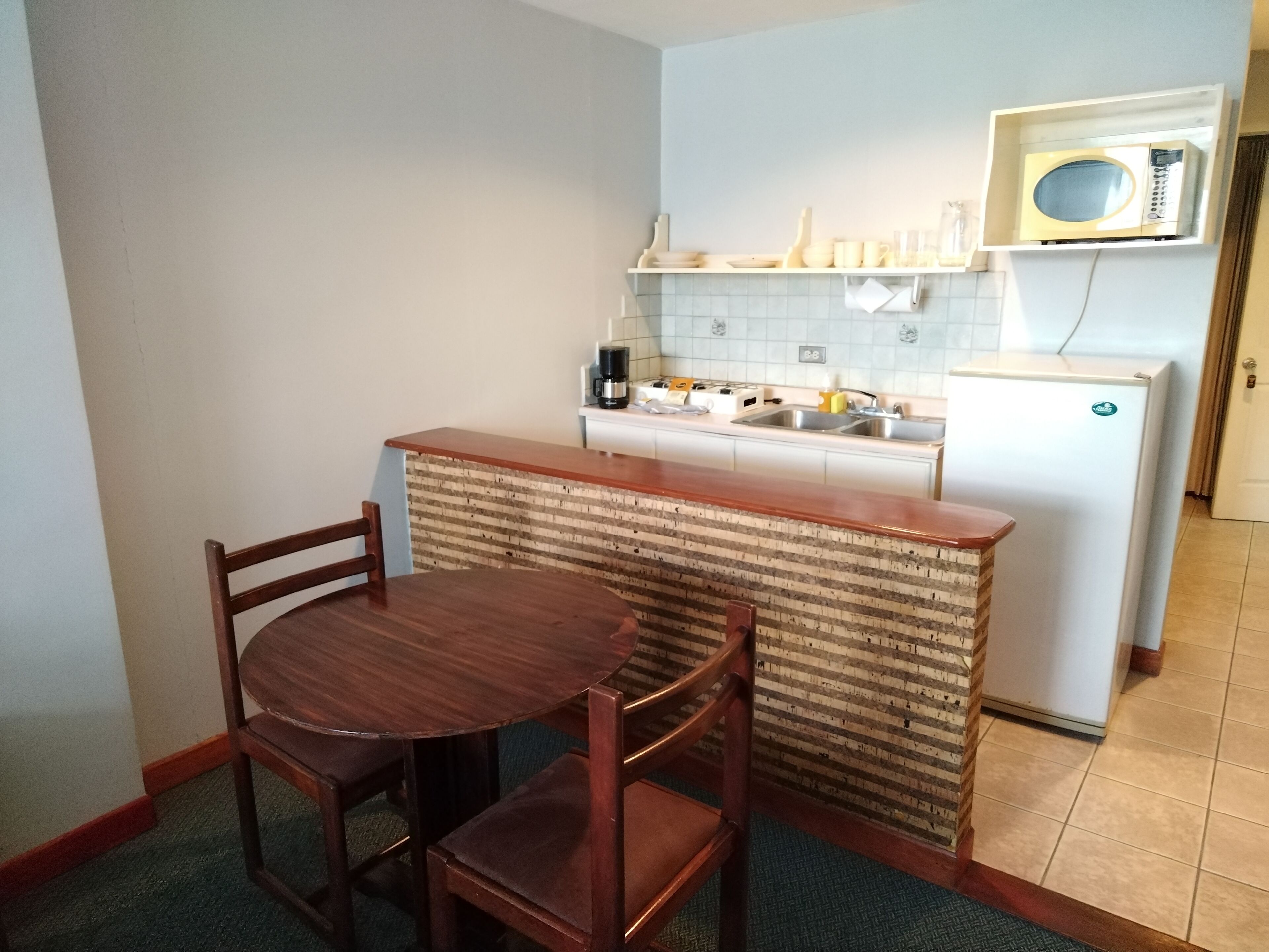 Cocina compacta con una mesa y sillas de madera, un microondas y un refrigerador pequeño.