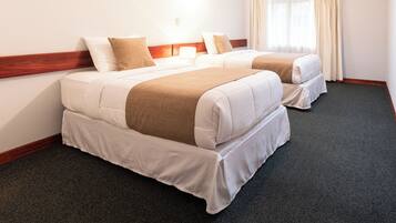 A hotel room with two beds, a ceiling fan, a window with curtains, and a carpeted floor.