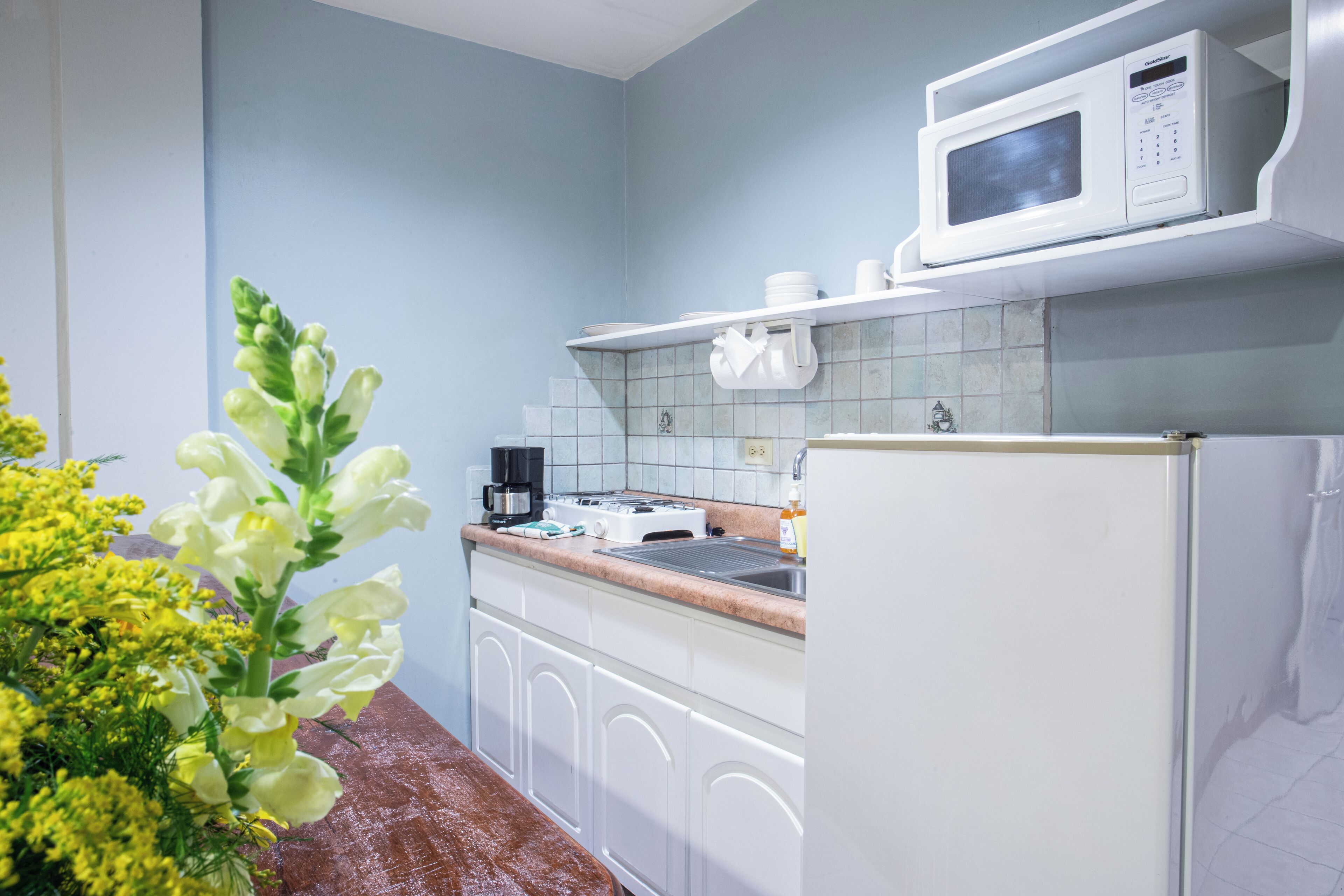 Una cocina con gabinetes blancos, microondas, estufa y refrigerador.