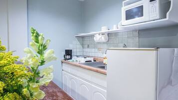 Una cocina con gabinetes blancos, microondas, estufa y refrigerador.