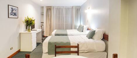 A hotel room with two beds, a small table with a tray of items, a desk with a vase of flowers, and a picture on the wall.