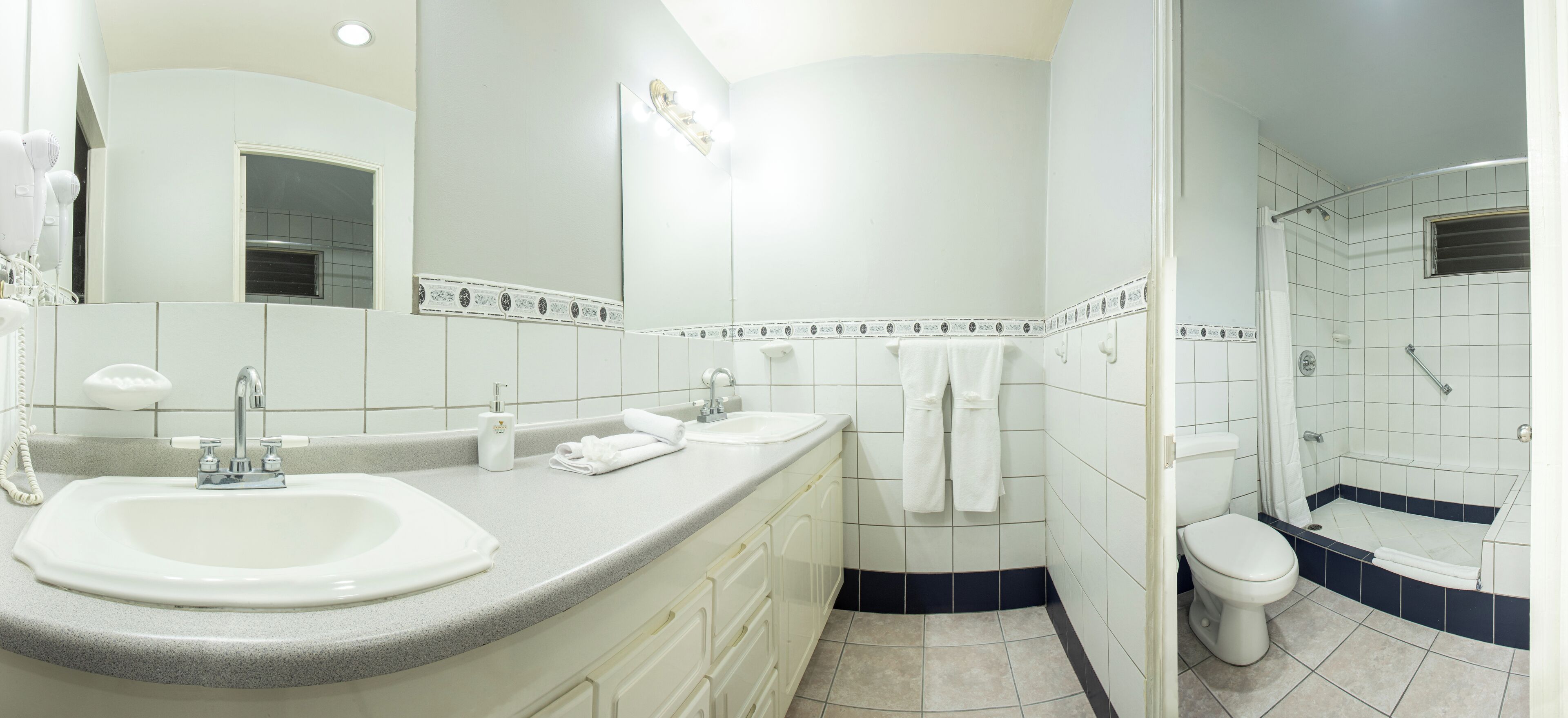 Un baño moderno con dos lavamanos, un espejo grande, una ducha y un inodoro.