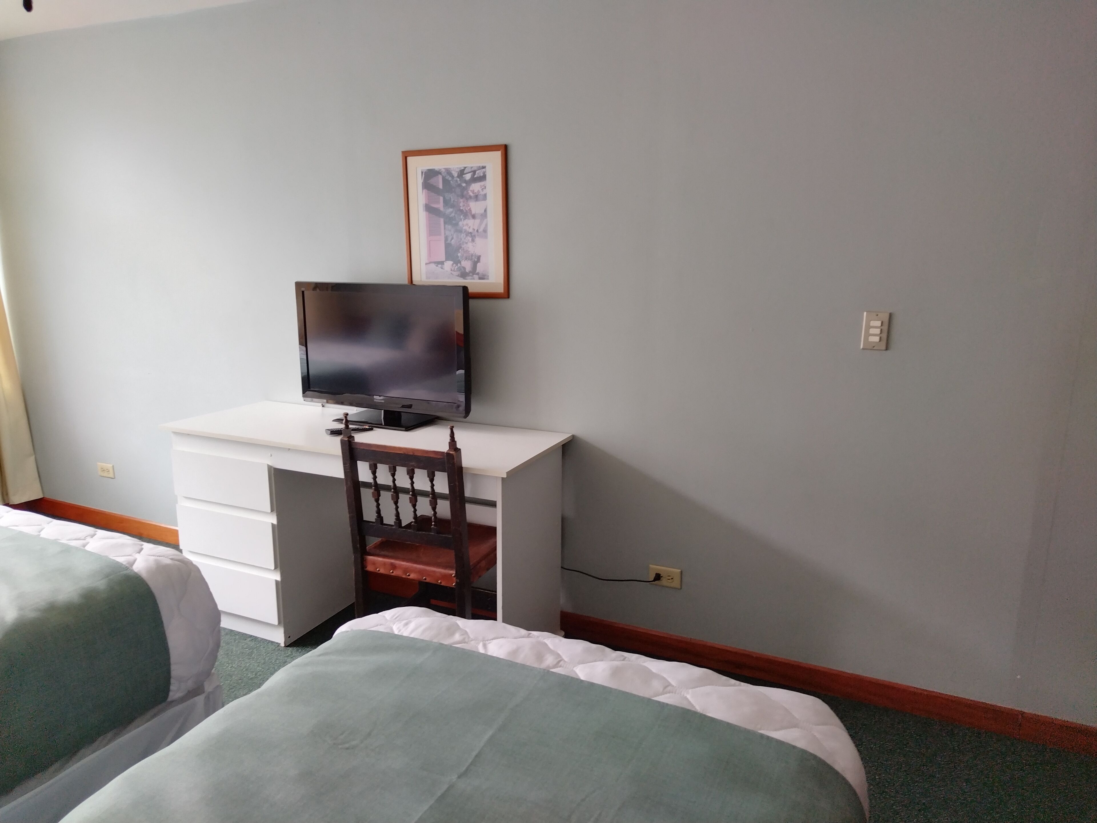 A hotel room with a bed, a desk with a television, and a chair.