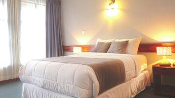 A hotel room with a bed, a ceiling fan, a nightstand with a lamp, and a window with curtains.