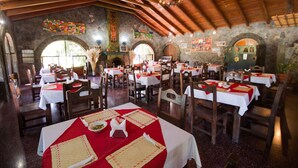 Un ristorante con diversi tavoli, sedie di legno e una parete in pietra con finestre ad arco.