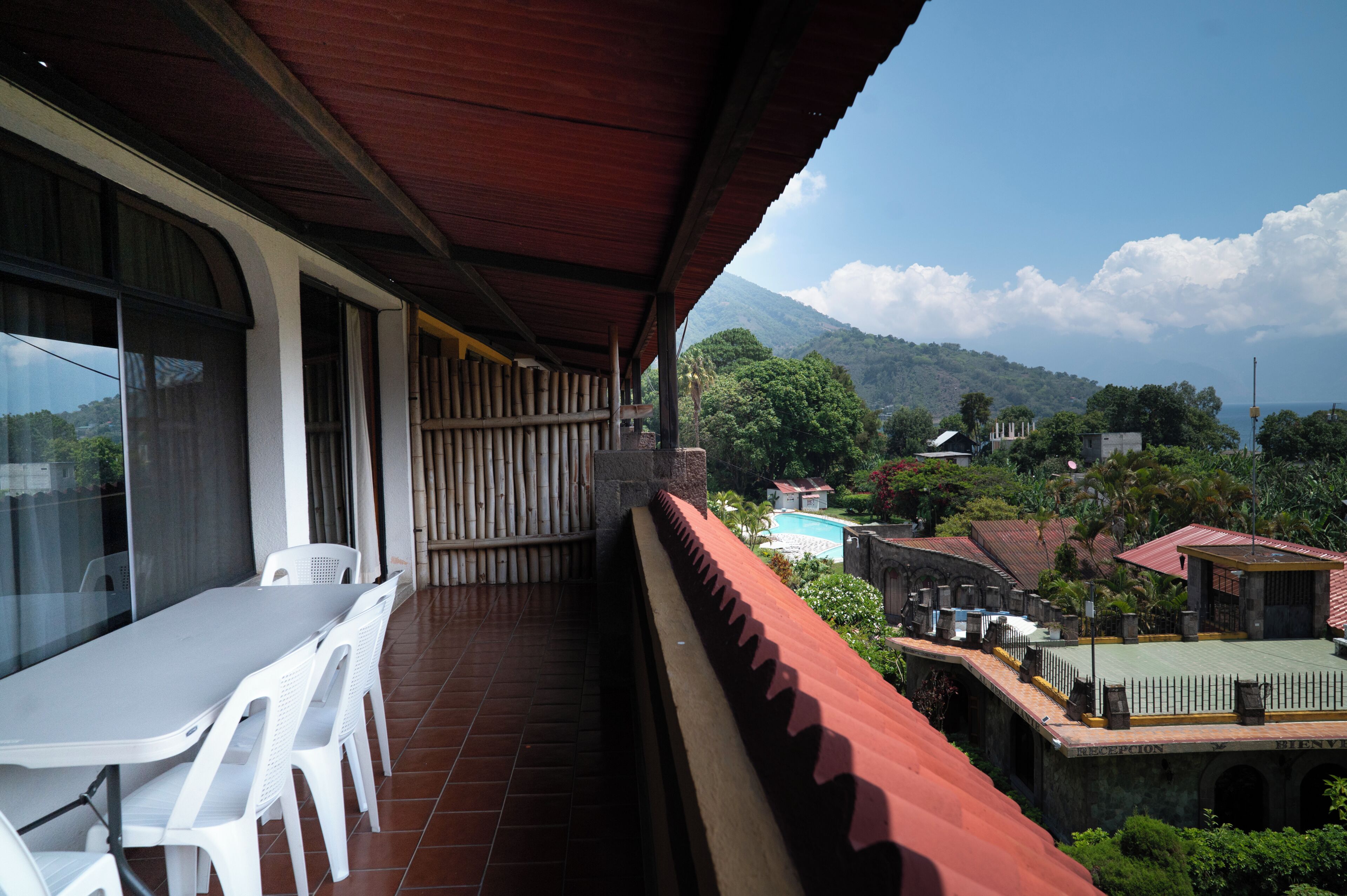 A balcony with a table and chairs, a red roof, and a view of a mountainous landscape.