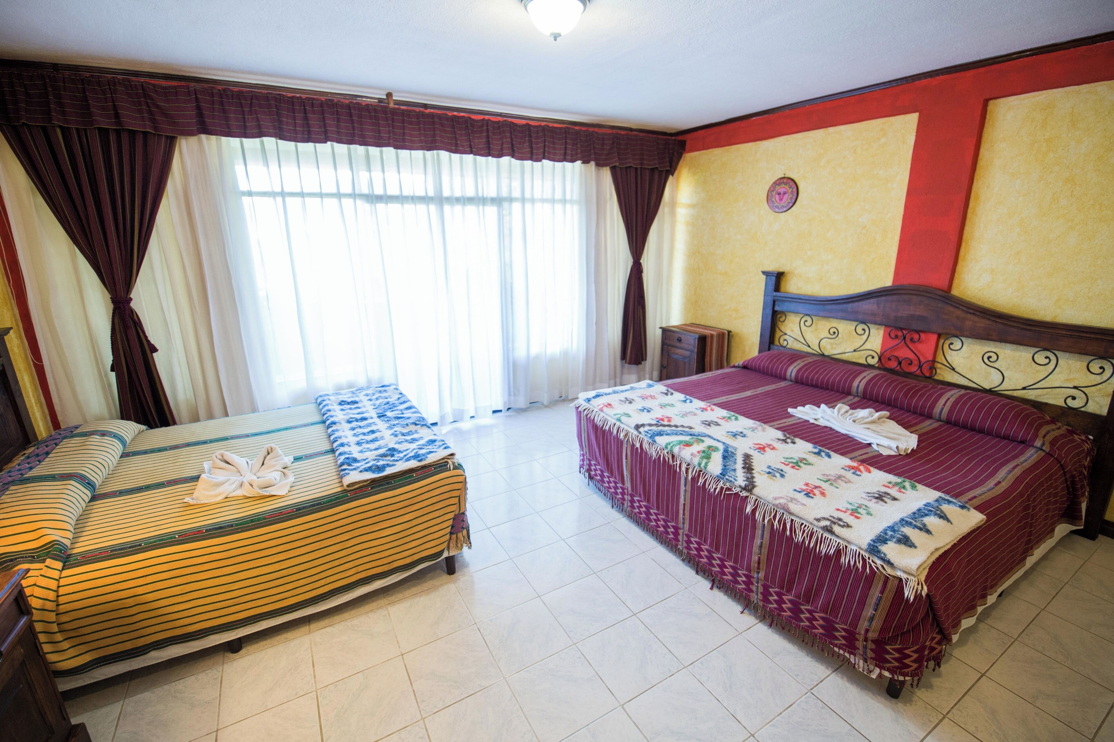 Habitación de hotel con dos camas, una mesita de noche, un reloj de pared y una ventana con cortinas.