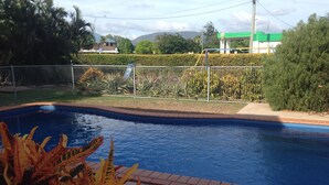 Una piscina con borde de ladrillo, rodeada por una cerca metálica y diversas plantas.