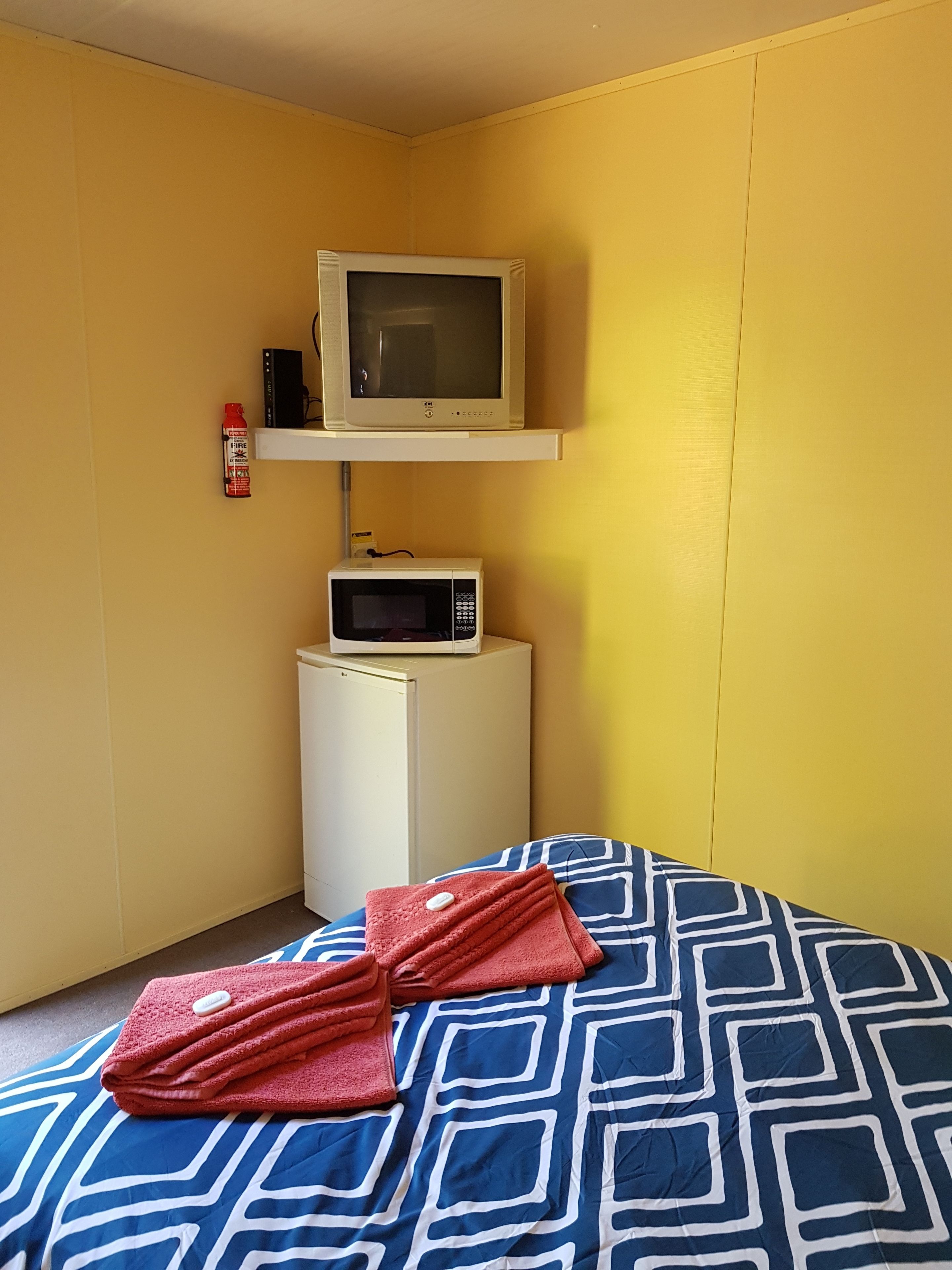 A hotel room with a bed, a microwave, a television, and a small white cabinet.