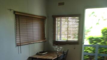 A bedroom with a bed, a desk, and a chair. There is a window with blinds, and a door leading outside.