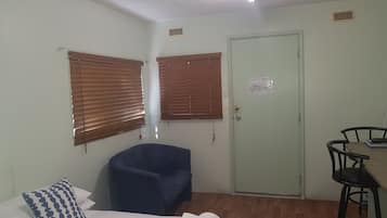 A room with a bed, a blue chair, a desk with a chair, and a door with an emergency exit sign.