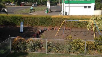 A gas station with a green canopy, a playground with a swing set, and a fenced area with plants.