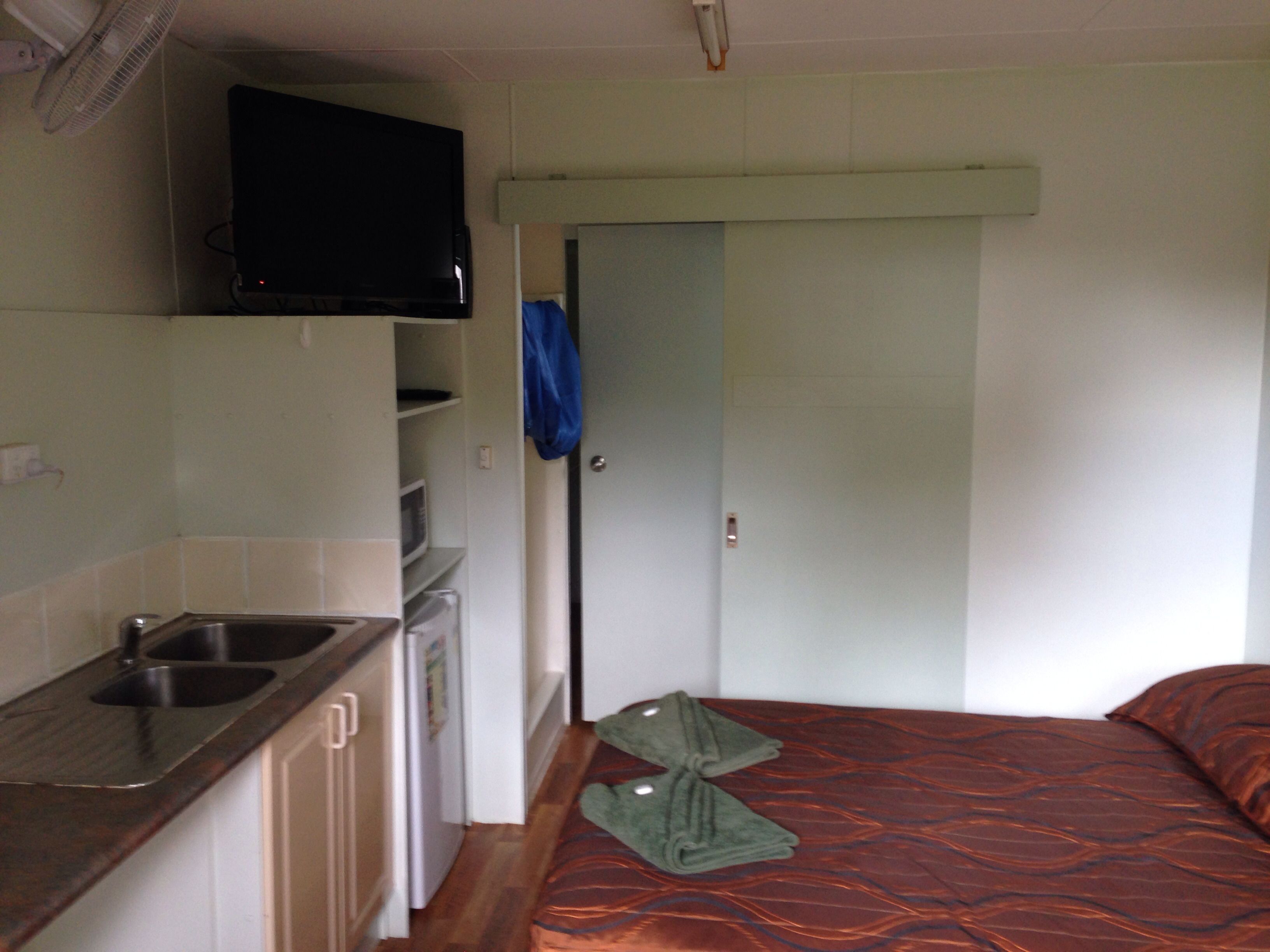 Habitación pequeña con kitchenette, una cama y una puerta que da a otra habitación.