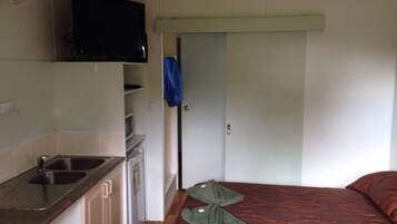 Habitación pequeña con kitchenette, una cama y una puerta que da a otra habitación.