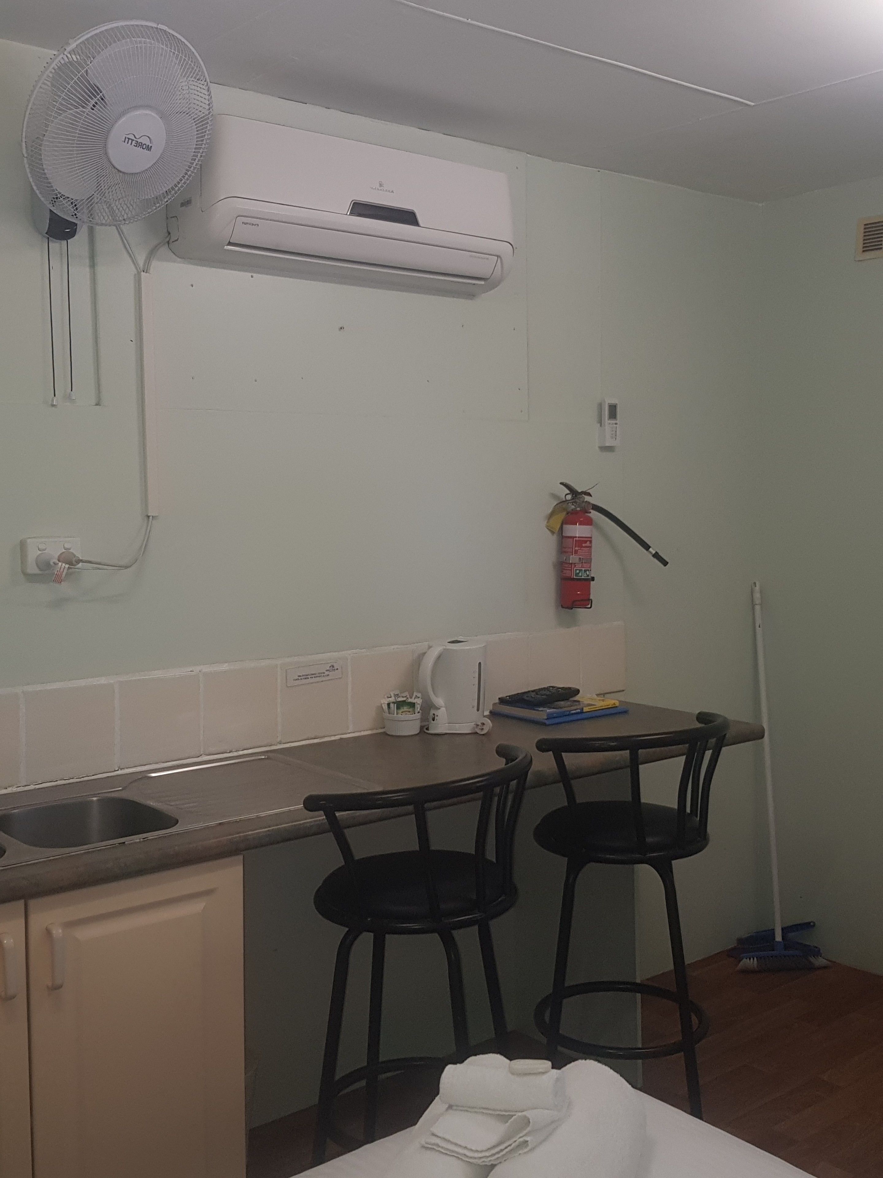 A small kitchenette with a fan, an air conditioner, a fire extinguisher, and a coffee maker.