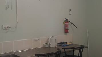 A small kitchenette with a fan, an air conditioner, a fire extinguisher, and a coffee maker.