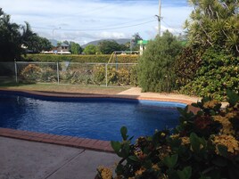 Una piscina con borde de ladrillo, rodeada de vegetación y una valla.