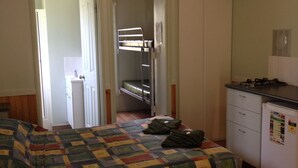 Una habitación pequeña y acogedora con una cama individual alta y baja, un kitchenette y una puerta que da al baño.