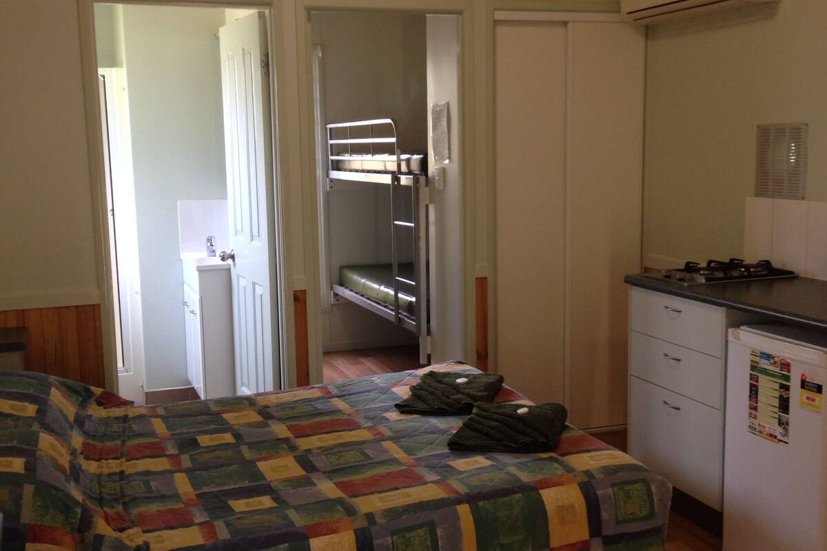 A small, cozy room with a bunk bed, a kitchenette, and a door leading to a bathroom.