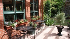 A patio with outdoor seating, brick walls, large windows, and potted plants. - The Grand Hotel Nanaimo (Nanaimo)