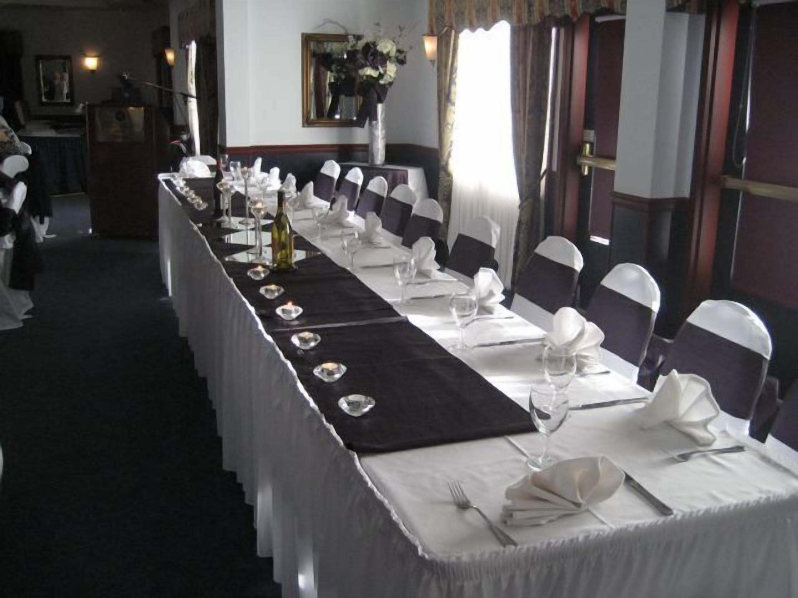 A long dining table set with white tablecloths, black chair sashes, and candles.