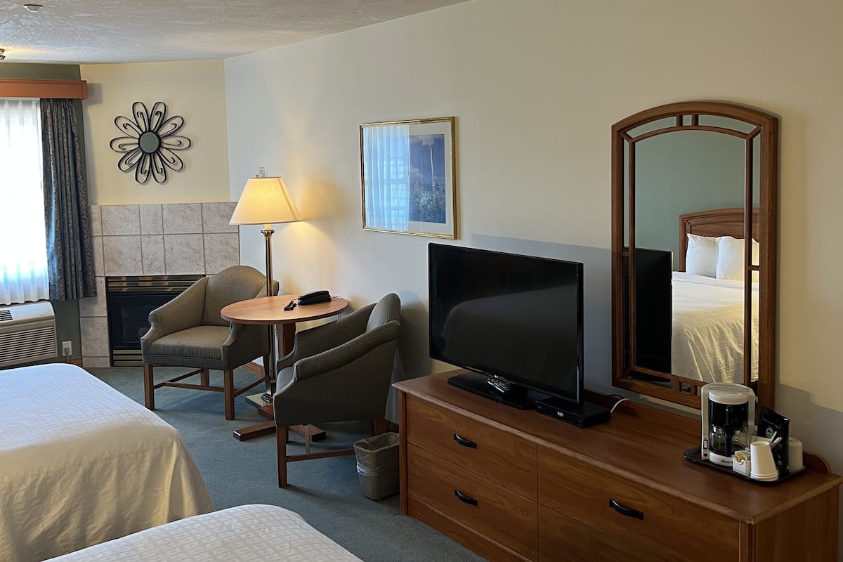 Hotelkamer met twee bedden, een televisie, een bureau met lamp, een stoel, een openhaard en een spiegel.
