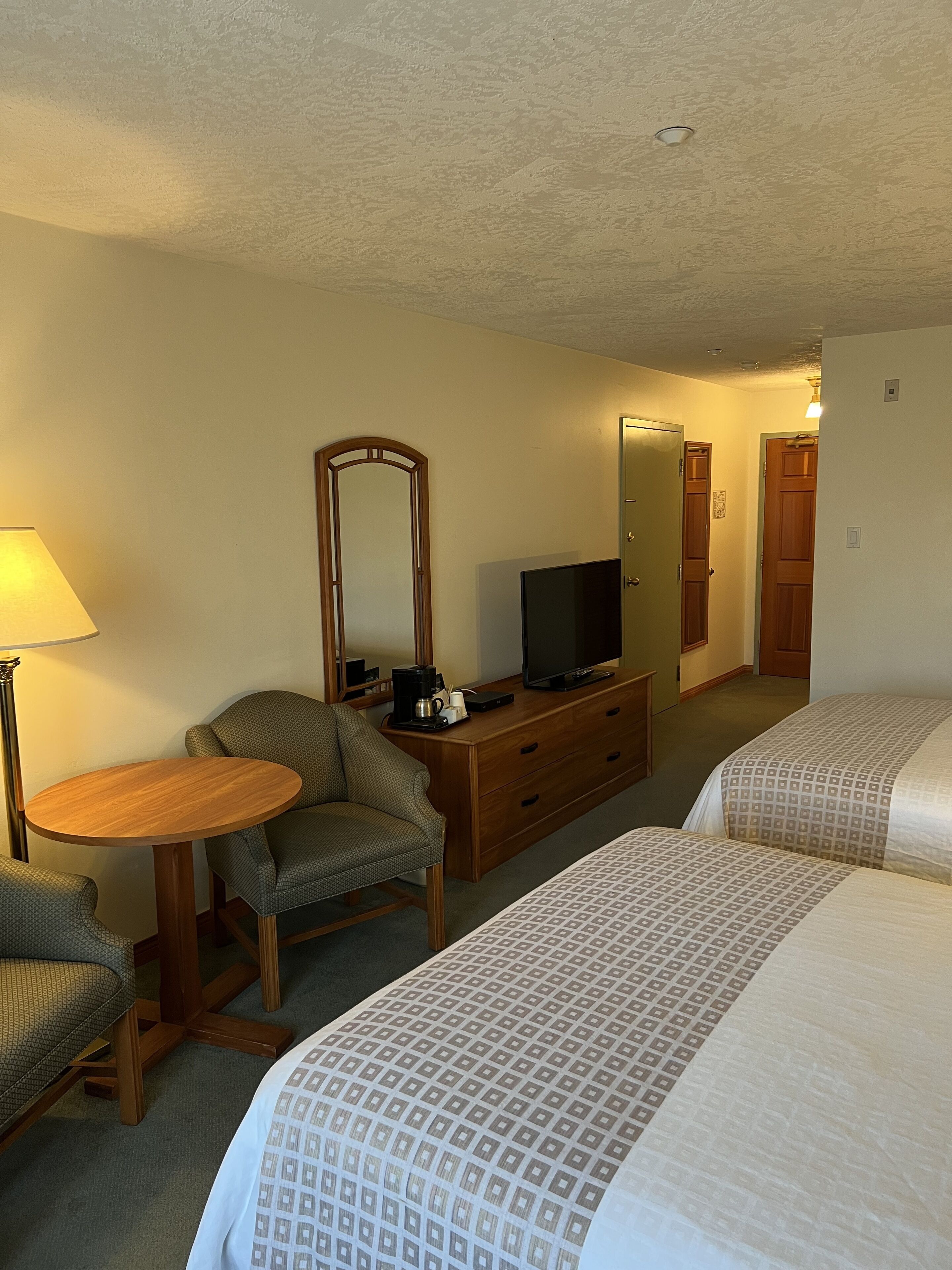 A hotel room with two beds, a desk with a lamp, a dresser, a television, and a mirror.