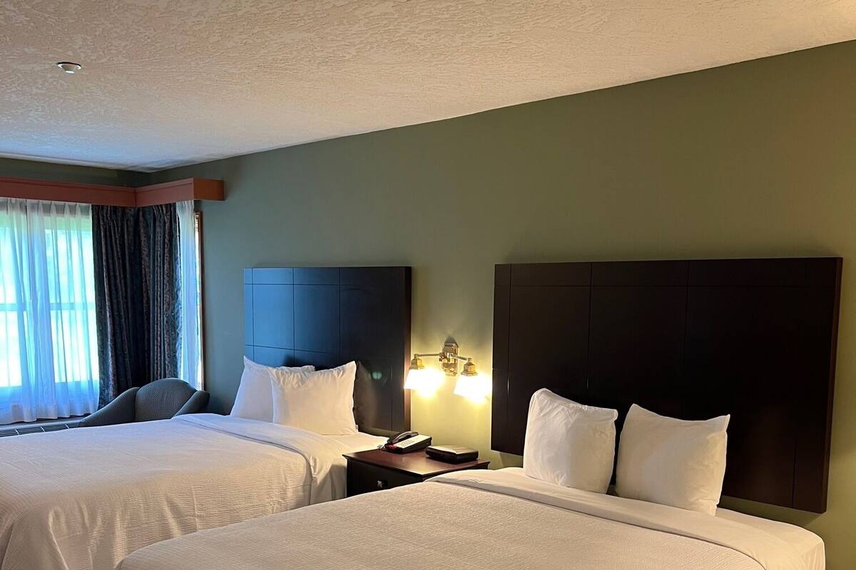 Een hotelkamer met twee bedden, een nachtkastje met een lamp en een raam met gordijnen.