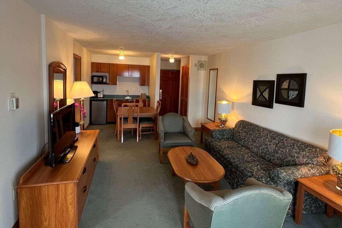 Een woonkamer met een bank, fauteuil, salontafel en een tv-meubel. Achtergrond is een keuken met kastjes en een magnetron.